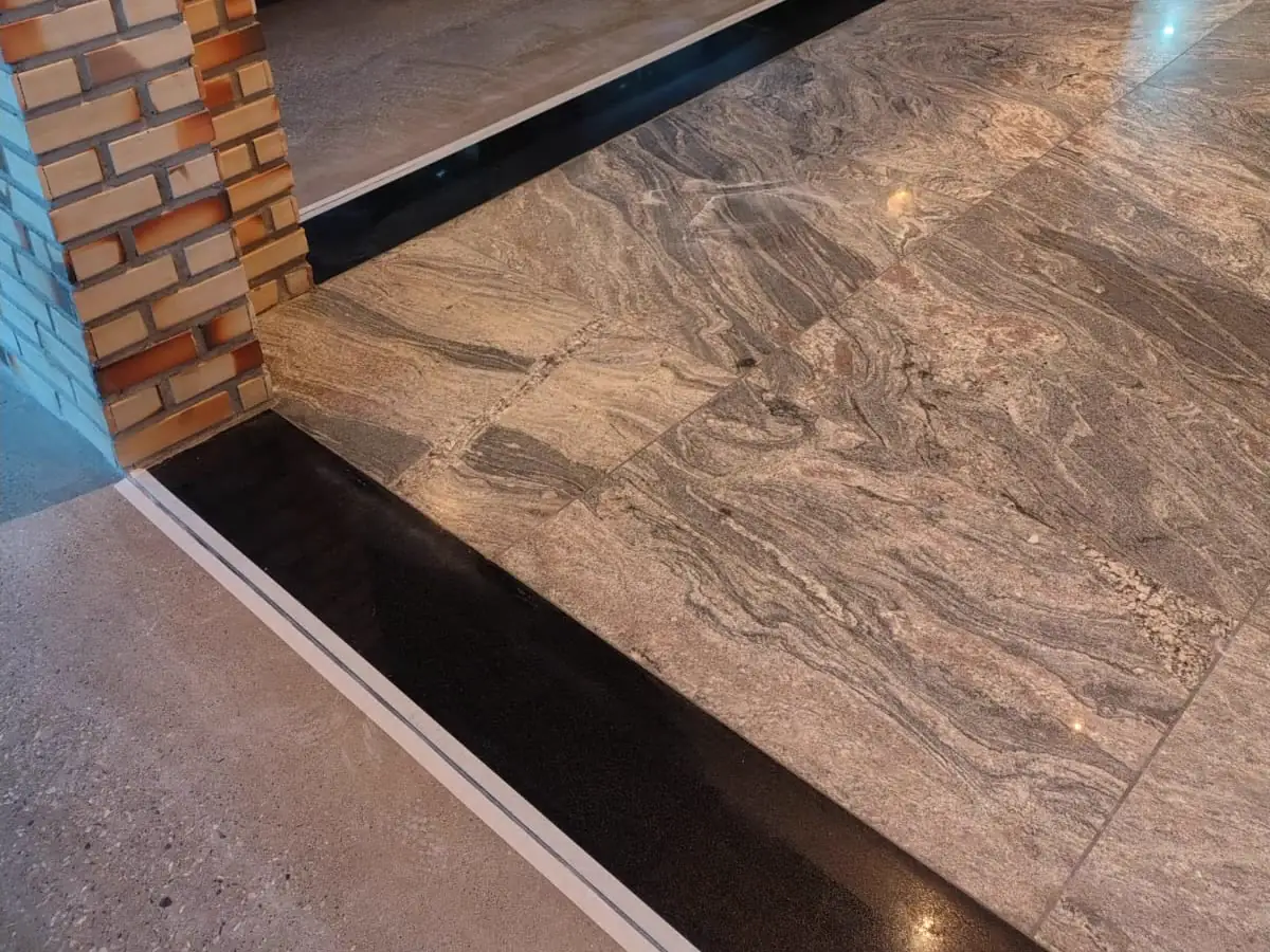 Piso de granito polido pela MG, com veio natural marcado, encontrando faixa de concreto polido