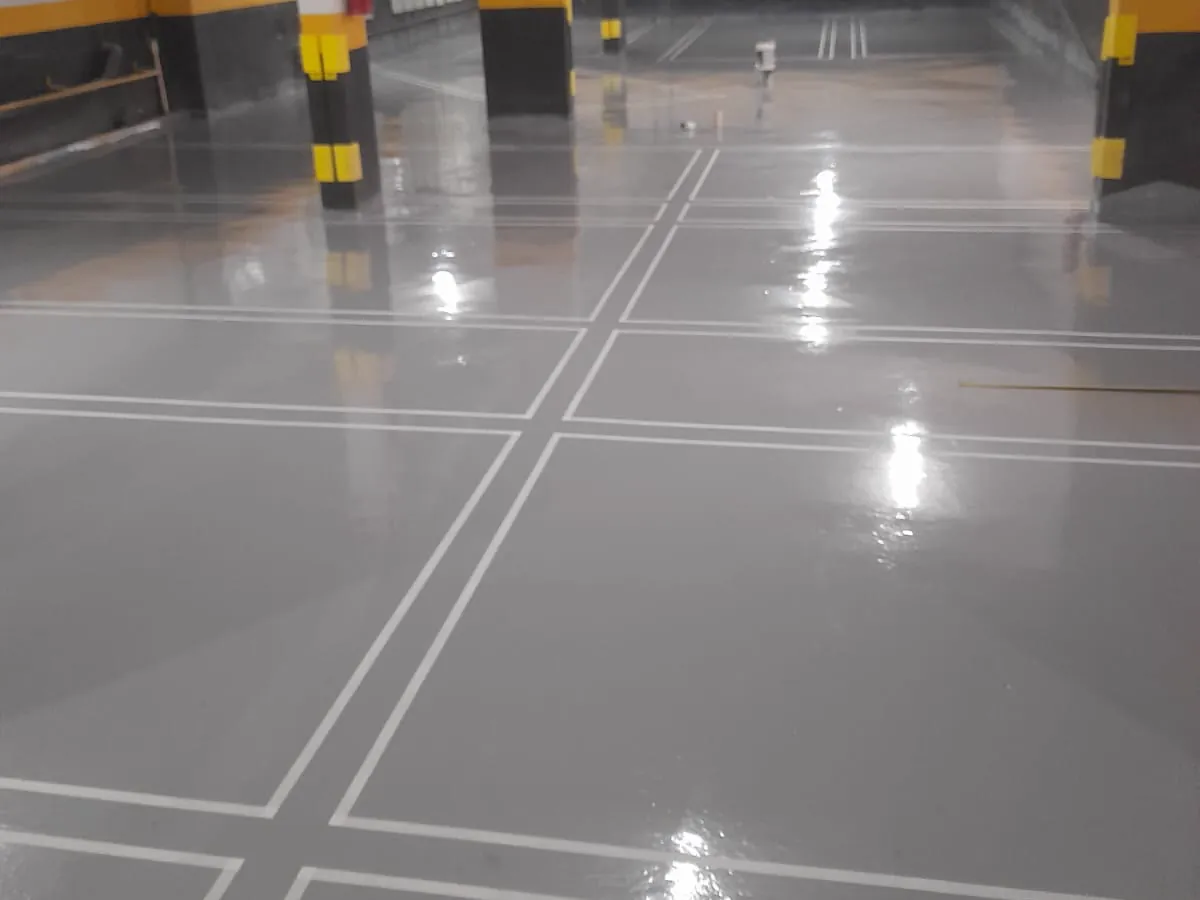 Estacionamento coberto com vagas demarcadas pela MG, faixas brancas contínuas sobre piso cinza e colunas sinalizadas em amarelo e preto
